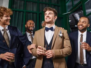 bachelor party, cheerful interracial men congratulating friend in bar, best men and groom in suits