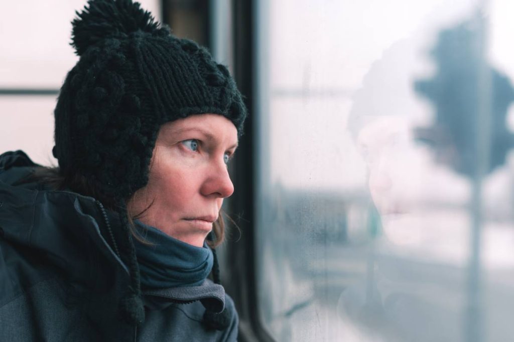 Sad woman on the bus looking through window at the street on cold winter day