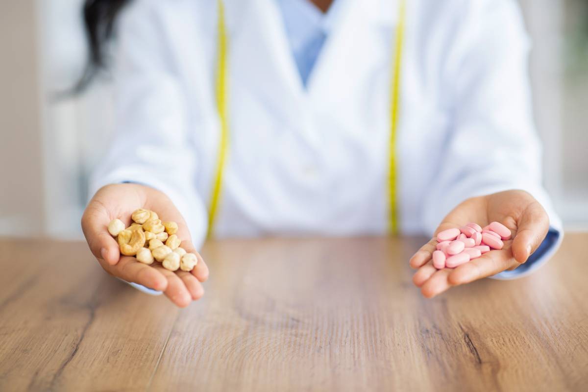 Healthy eating concept. Unrecognizable female dietitian holding pills and cashew nuts at table in clinic, closeup