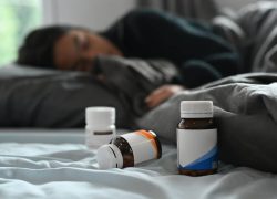 Selective focus on pill bottles and ill little girl lying in bed under blanket with high fever.