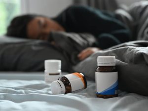 Selective focus on pill bottles and ill little girl lying in bed under blanket with high fever.