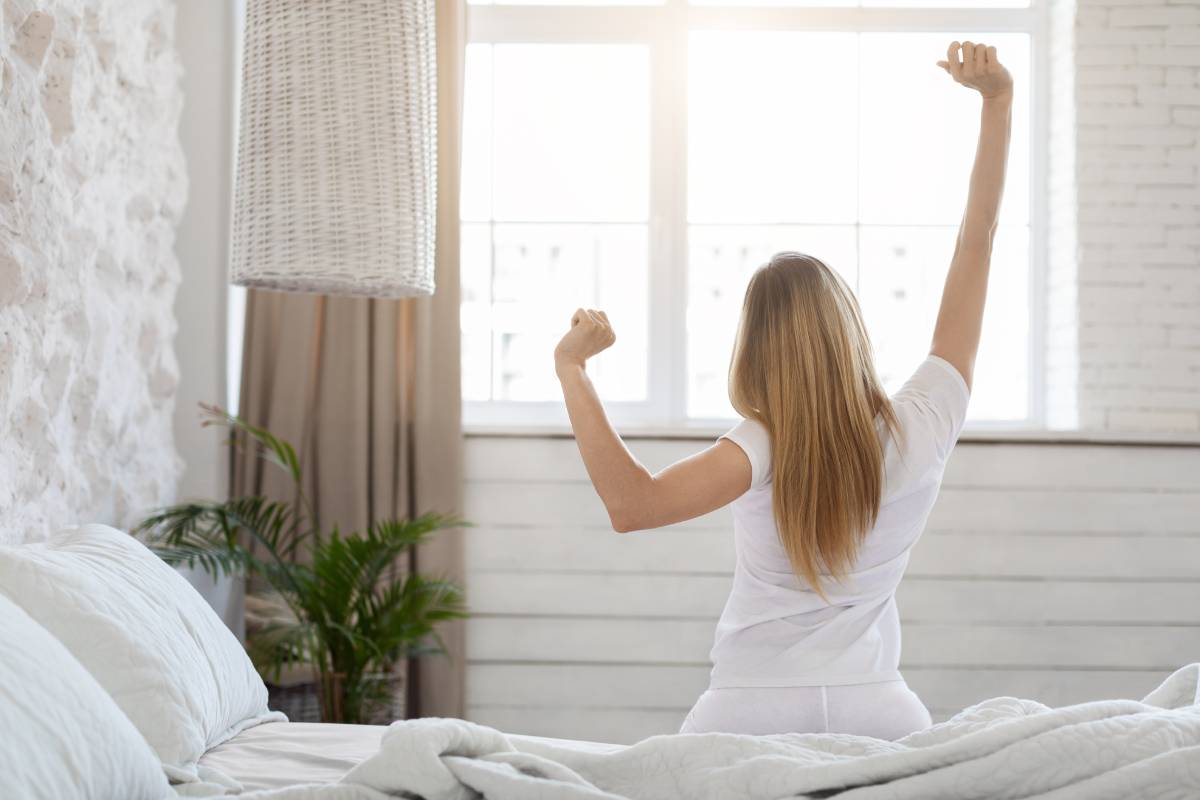 Unrecognizable blonde woman enjoying happy morning, stretching in bed