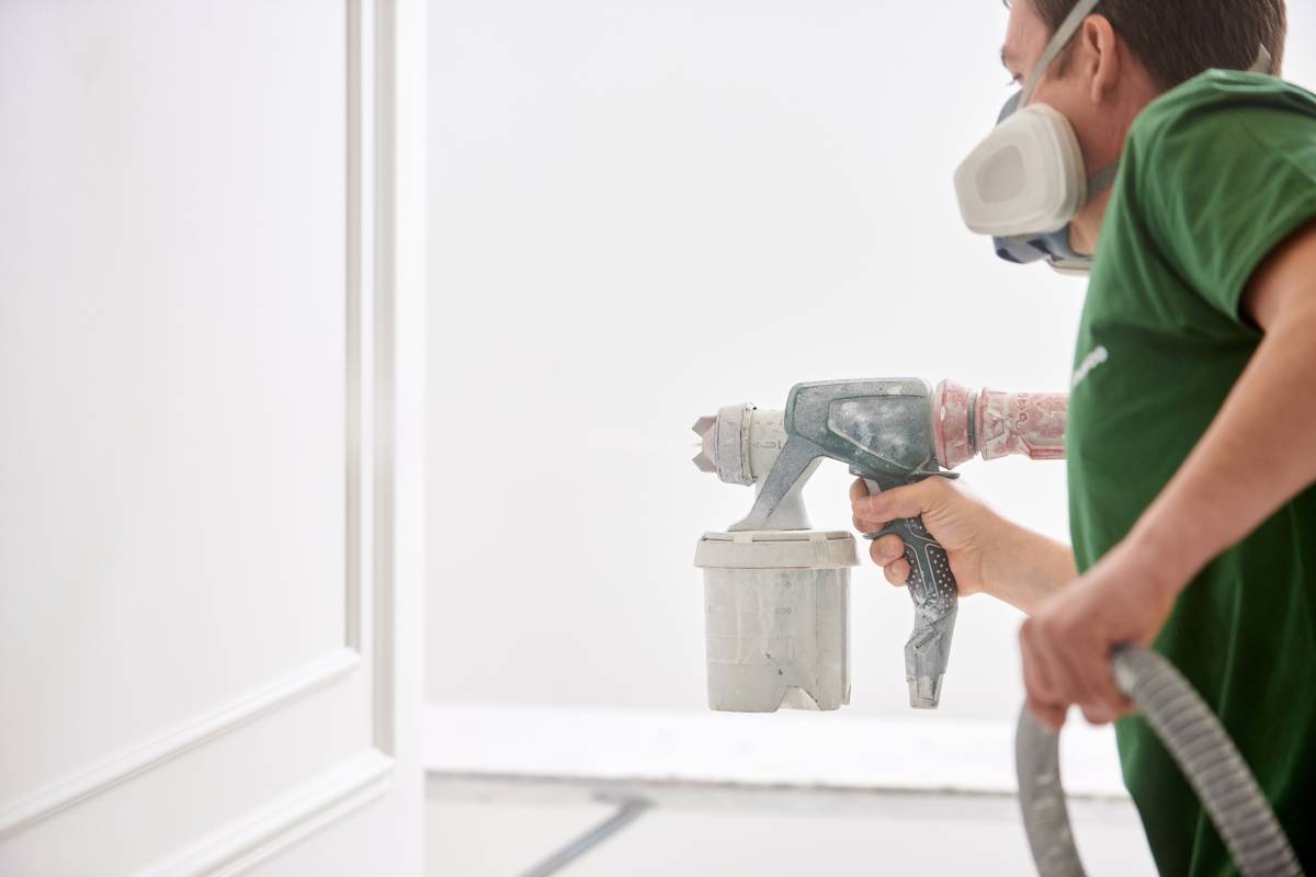 Worker painting wall with spray gun in white color.