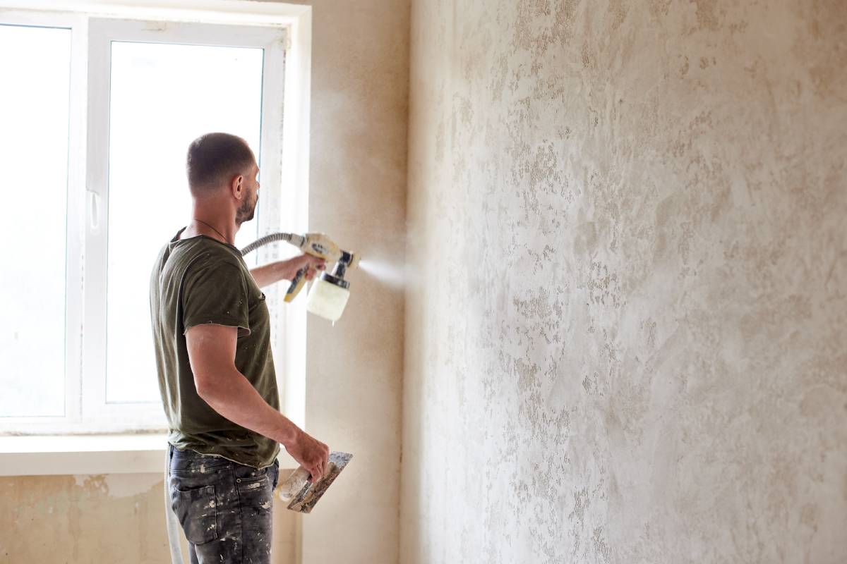 Worker painting wall with spray gun. Man with beard at the apartment