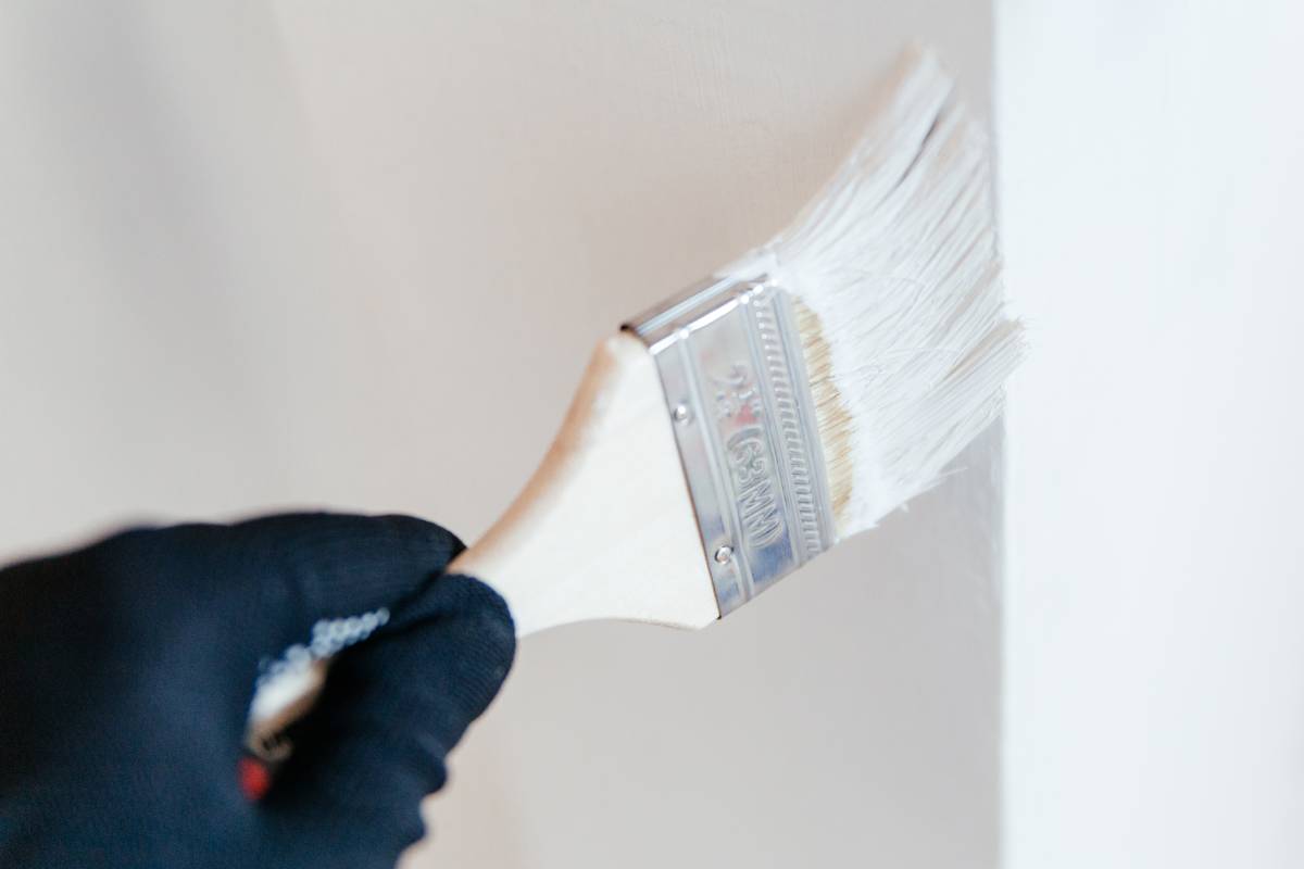 Close-up of a worker's hand with a brush painting a wall with white paint.