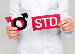 cropped view of doctor in white coat holding gender symbols and std lettering isolated on grey