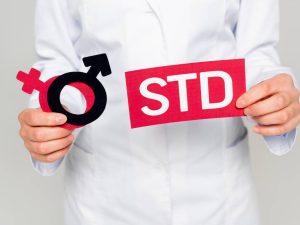 cropped view of doctor in white coat holding gender symbols and std lettering isolated on grey