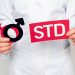 cropped view of doctor in white coat holding gender symbols and std lettering isolated on grey