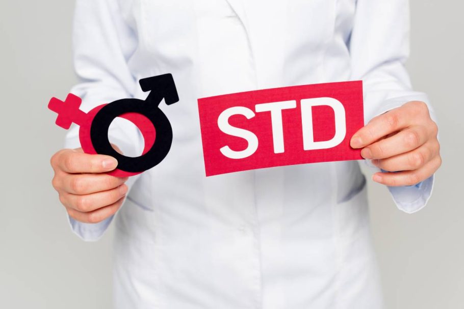 cropped view of doctor in white coat holding gender symbols and std lettering isolated on grey