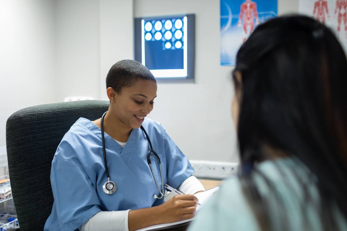 Front view of mixed-race female doctor giving prescription to pregnant woman at desk in hospital