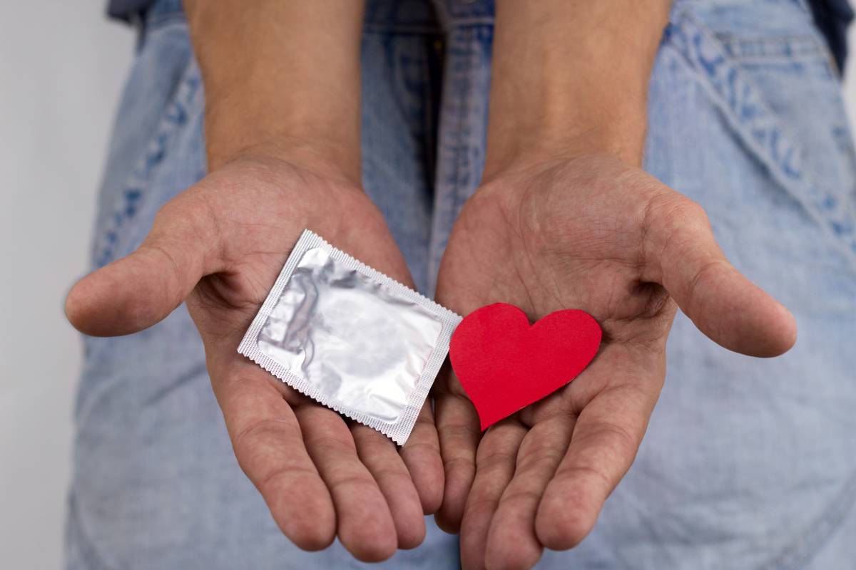 close up of male hands holding a condom pack  and a red heart, safe sex concept