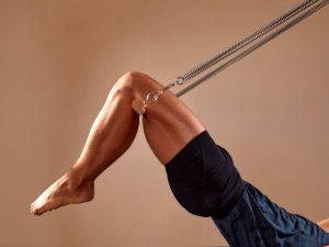 Handsome pilates male instructor performing stretching balance fitness exercise on small barrel equipment, at the pilates studio modern onterior indoor.