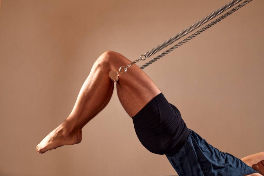 Handsome pilates male instructor performing stretching balance fitness exercise on small barrel equipment, at the pilates studio modern onterior indoor.