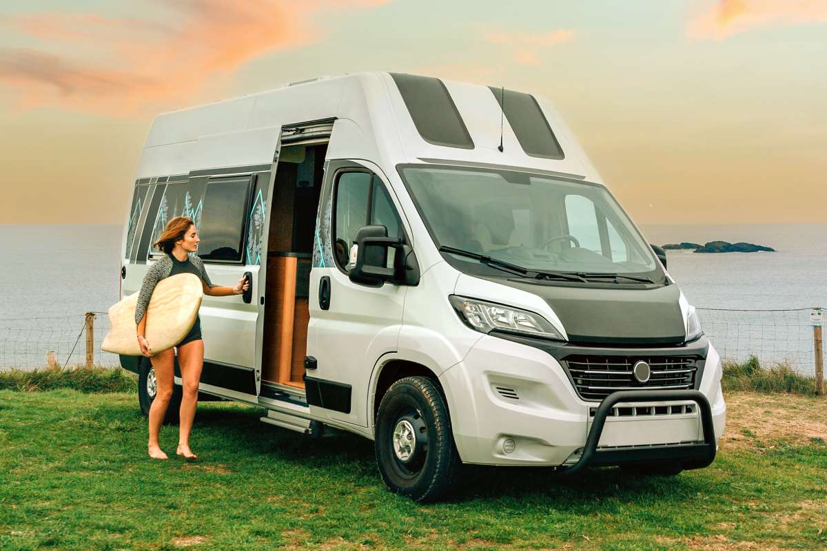 Young woman with wetsuit and surfboard closing the door of her camper van to go surfing